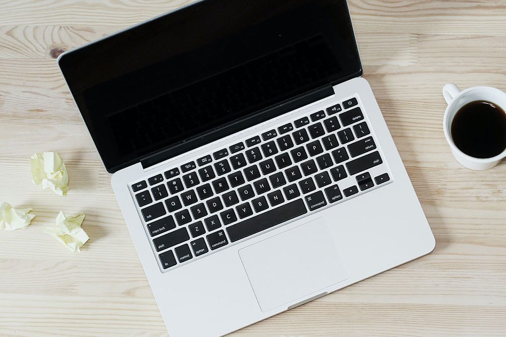 Laptop, coffee and notes on a wooden desk seen from above